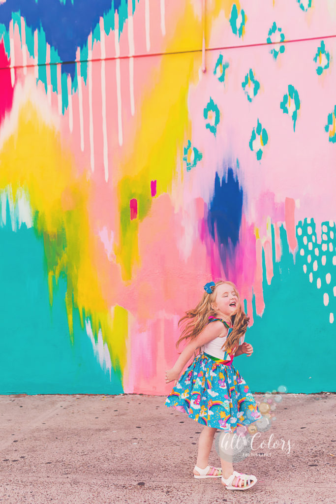 Girl wearing a rainbow dress in front of a very colorful mural in Downtown San Diego.