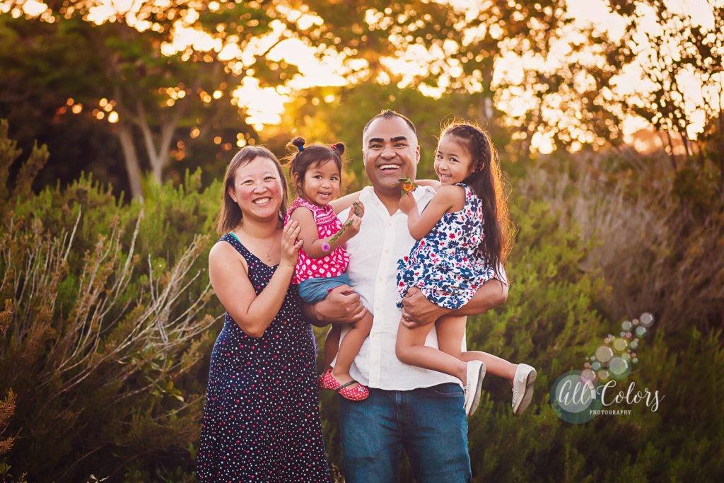 A family of 4: mom, dad, and two young daughters smiling 