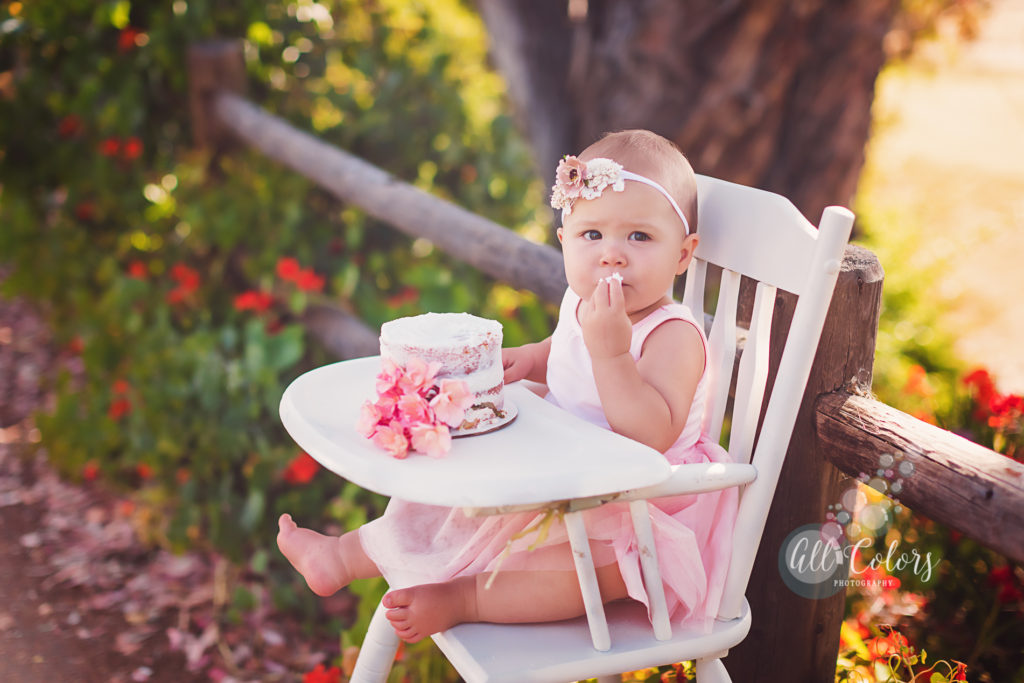 Baby girl eating a white cake in a garden.