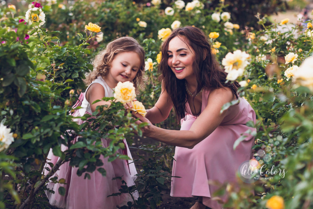 mother and daughter looking at a yellow rose in a rose garden