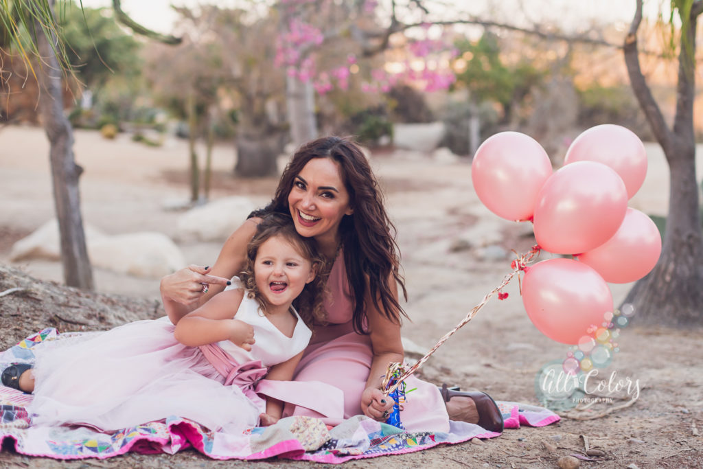 mother and daughter laying on quilt blanket holding pink balloons