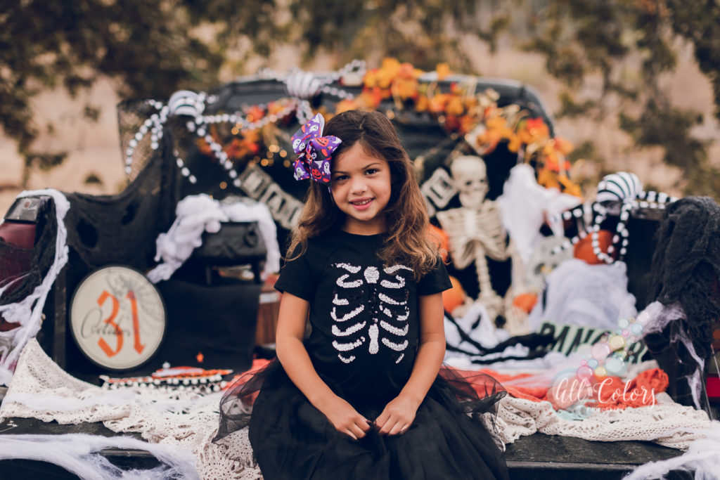 Girl with a big purple bow sitting on the back of a pick up truck decorated for Halloween