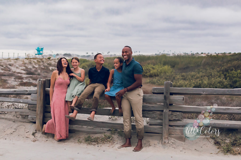 Blended family sitting on a fence at the beach and laughing at something funny