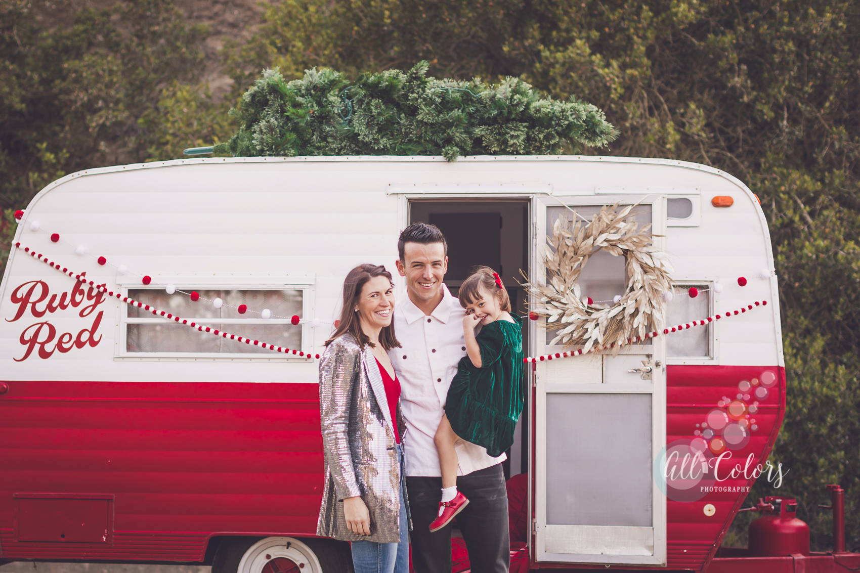 a red and white camper decorated for Christmas with a family standing in front of it.