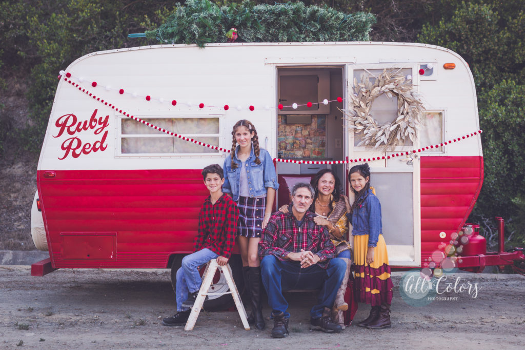 family of 5 sitting in front of a red camper decorated for Christmas.