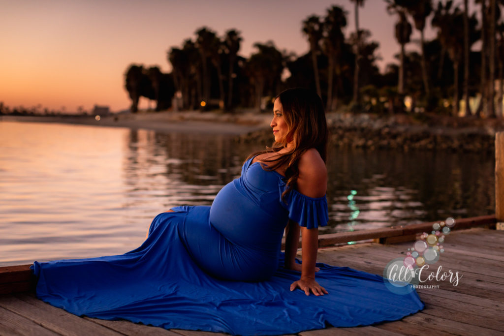 mom to be wearing blue dress sitting on a pier