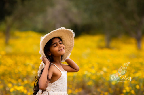 young girl holding her hat on a field of yellow wildflowers