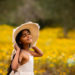 young girl holding her hat on a field of yellow wildflowers