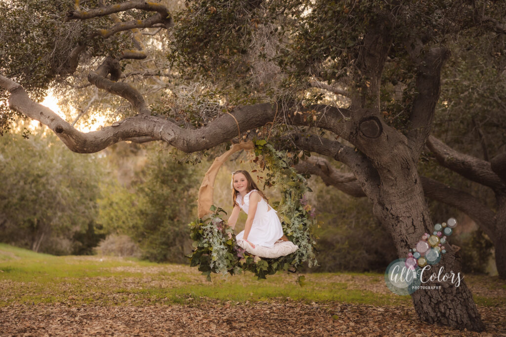 Girl on a Flower hoop hanging but a long branch.