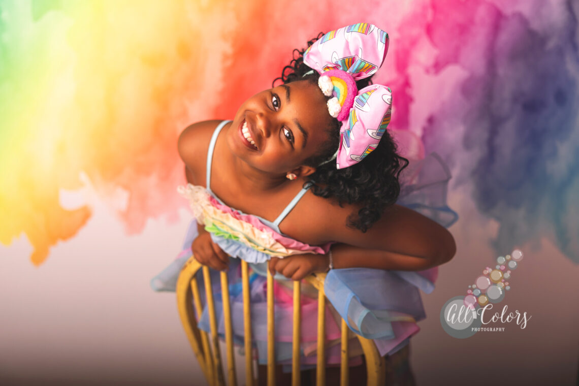 Black girl with a big bow on her head in front of a rainbow pastel backdrop